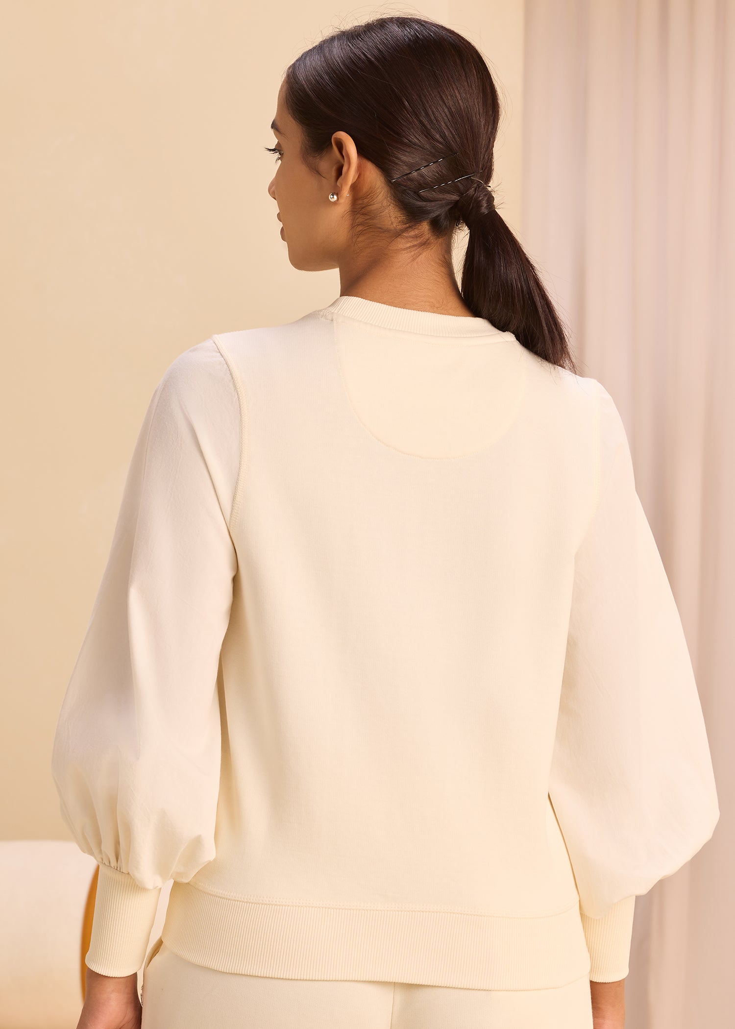 Young woman with braided hair standing and facing away while wearing a white long balloon sleeve top.