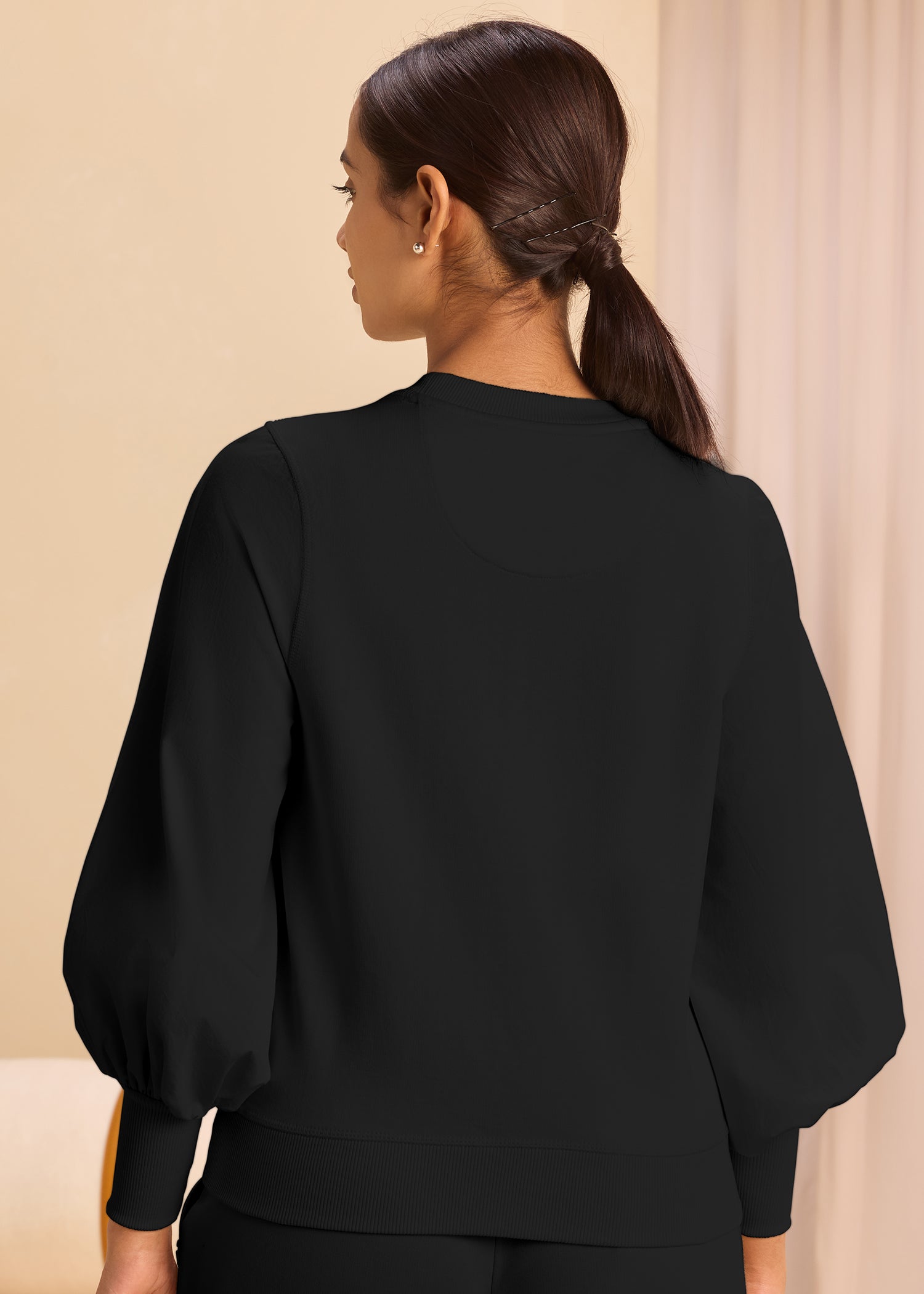A model showcasing the back pose of a trendy black sweatshirt with long sleeves and puffed shoulders, combining comfort and style effortlessly