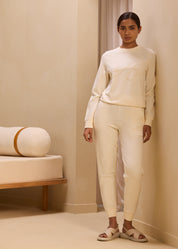 Model wearing a matching cream-colored jogger set with embroidered 'A' logo on the sweatshirt and pants, exuding a minimalist and cozy aesthetic in a neutral-toned room.